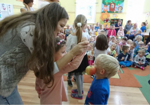 Chłopczyk próbuje jeść jabłko zawieszone na nitce bez pomocy rąk.