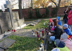 Nauczycielka z dziećmi zapala znicze przy grobie żołnierzy poległych w obronie naszego miasta.